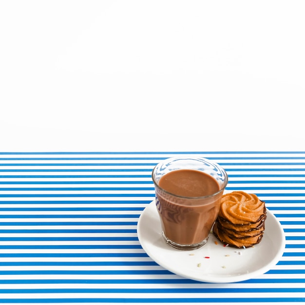 Free photo coffee glass and stack of cookies on plate over white and stripes backdrop