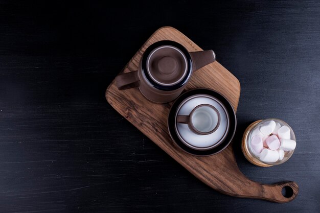 Coffee kettle with a cup and marshmallows on a wooden platter on a black.