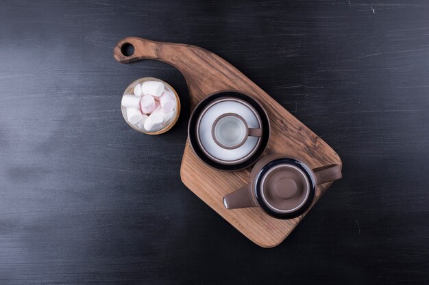 Coffee kettle with a cup and marshmallows on a wooden platter, top view.