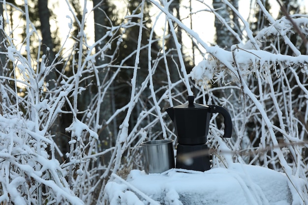 Coffee maker and metal cup on stump in winter day