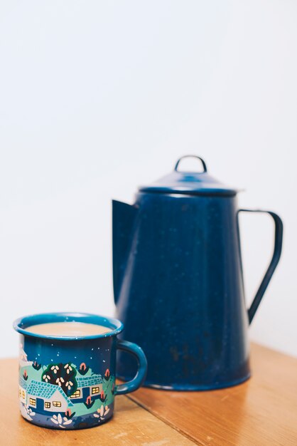 Coffee mug and blur teapot on wooden table against white backdrop