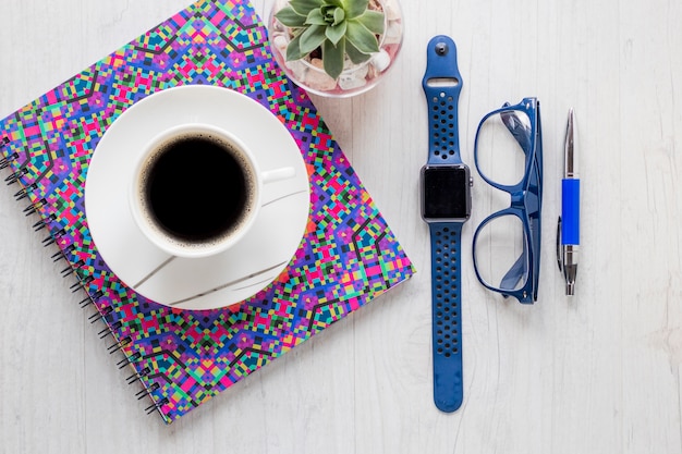 Coffee on notebook near accessories and plant