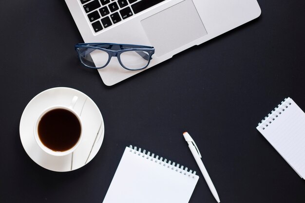 Coffee and notepads near glasses and laptop