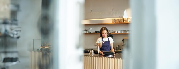 無料写真 カフェで注文を受けるためにタブレットを使用してカウンターの後ろで働く笑顔の韓国人バリスタ女性