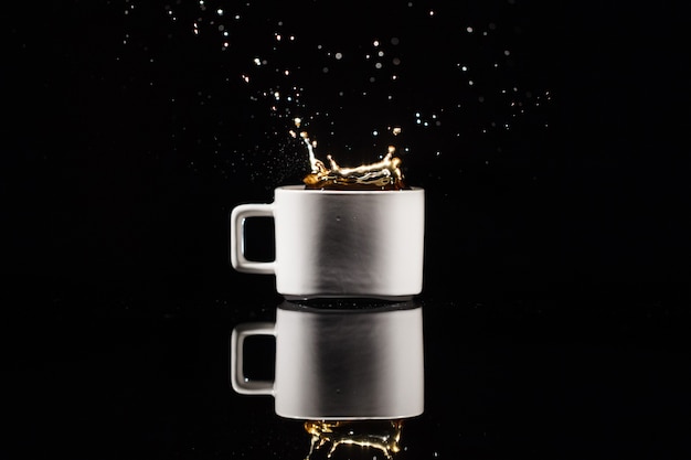 Coffee splashes in white cup on black background