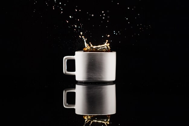 Coffee splashes in white cup on black background