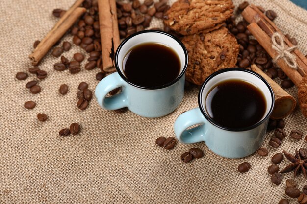 Coffee with coffee beans, cookies and cinnamon on a burlap.