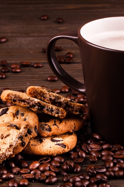 Il caffè con il latte si leva in piedi sui chicchi di caffè con i biscotti del cioccolato