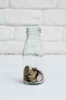 Foto gratuita monete raccolte nella bottiglia di vetro del latte contro il muro bianco