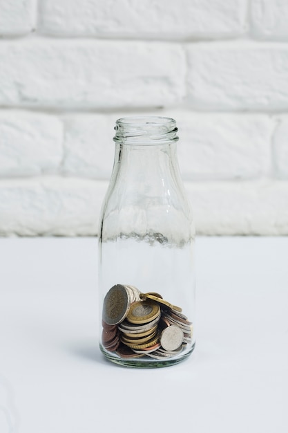 Монеты, собранные в бутылке с молочным стеклом против белой стены