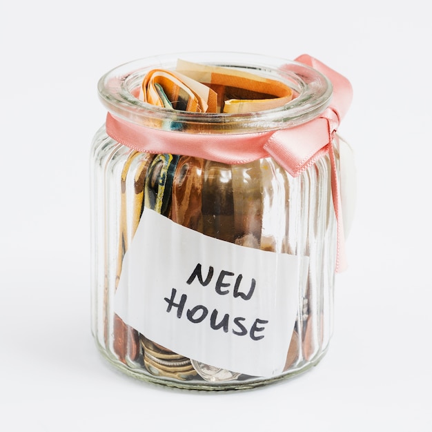 Монеты и ноты евро в стеклянной банке, украшенной розовой лентой, собранной для нового дома