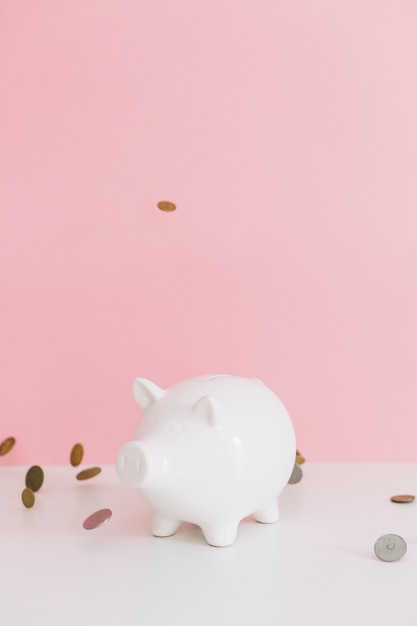 Coins falling over the white piggybank over the desk