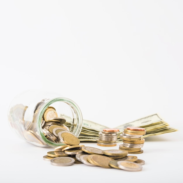 Coins scattered from jar with paper money on table