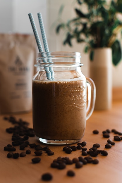 Cold coffee with blue straws surrounded by coffee beans