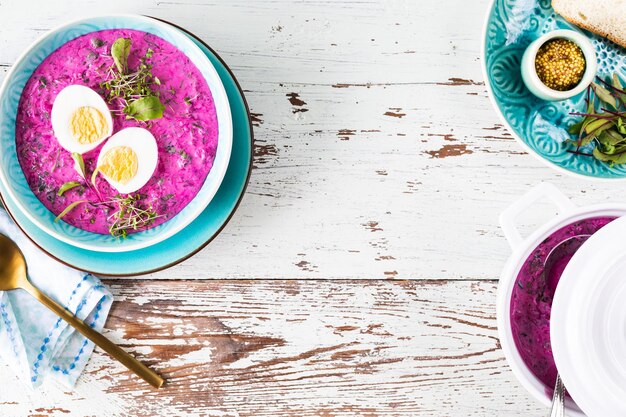 Cold soup made from beets cucumbers and garnished with an egg in a blue plate on a wooden background Top view