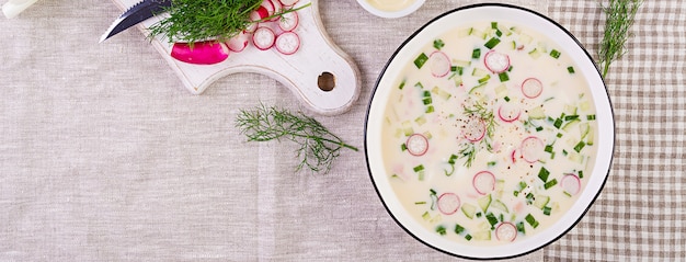 ボウルにヨーグルトと新鮮なキュウリ、大根、ジャガイモ、ソーセージの冷たいスープ。伝統的なロシア料理-オクロシカ。夏の冷製スープ。上面図。