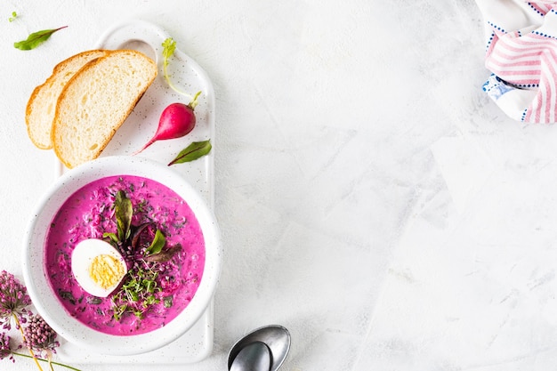 Cold summer soup of beets, cucumbers and eggs in a white plate on a white stone table. Top view. Copy space.