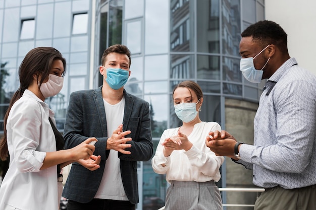 Colleagues disinfecting hands outdoors during pandemic while wearing masks