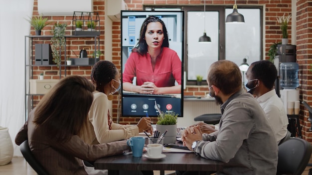 Colleagues meeting with woman on video call conference, using remote video teleconference on monitor. Business people working with online videoconference during covid 19 pandemic.