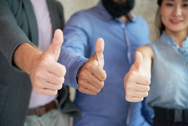 Colleagues posing together in office and showing thumbs up to camera