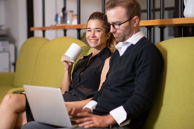 Colleagues relaxing and sitting on couch in office lobby. 