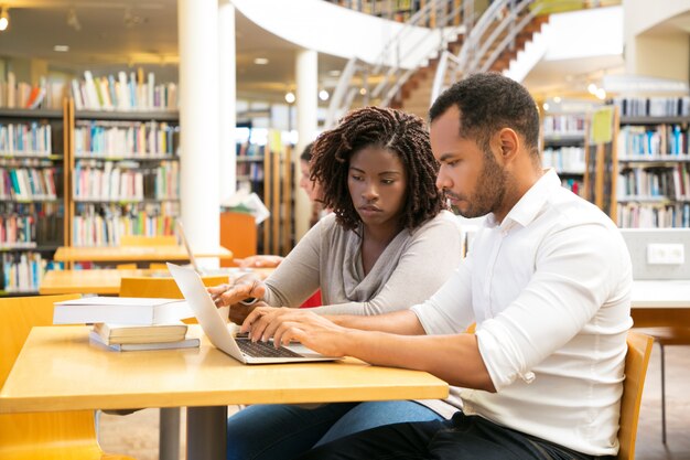 Colleagues sitting at library and using laptop