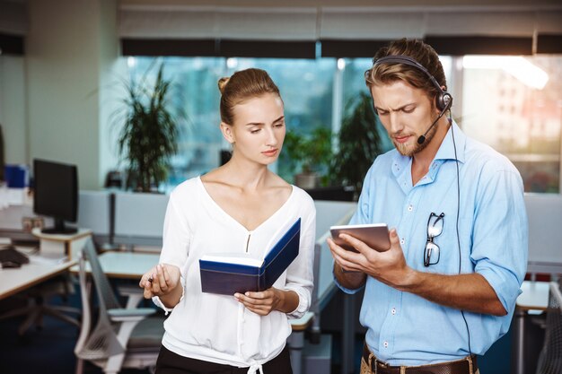 Colleagues smiling, speaking, holding tablet and notebook, over office