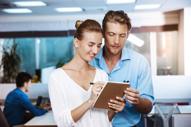 Colleagues smiling, speaking, looking at notebook, over office