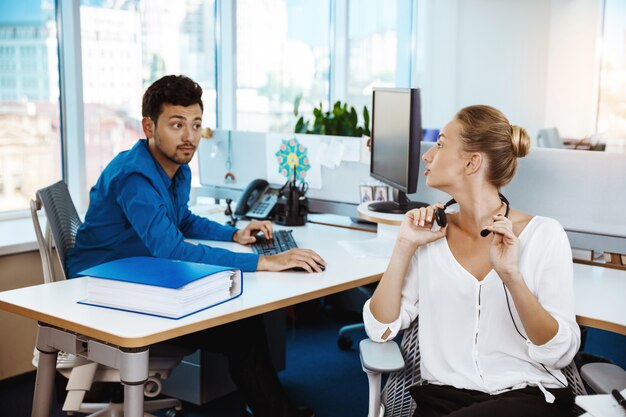 Colleagues speaking, consulting, sitting at workplaces over office