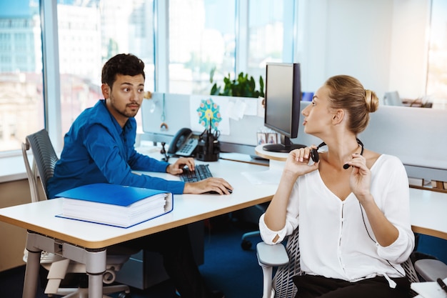 Colleagues speaking, consulting, sitting at workplaces over office