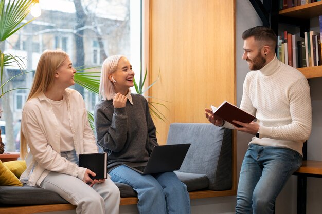 Colleagues studying in a library while using a laptop and notebooks