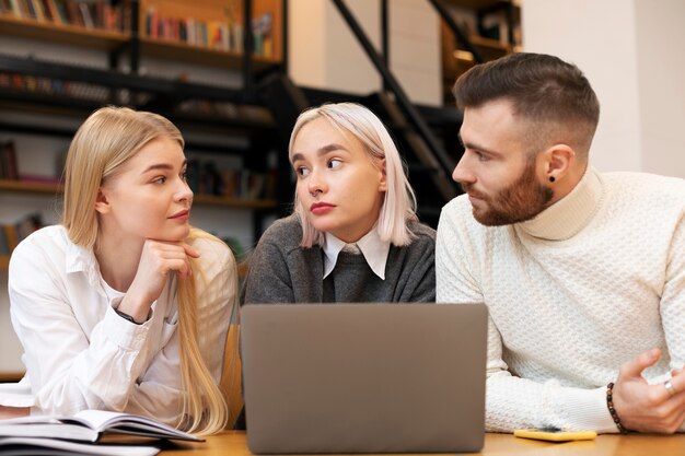 Colleagues talking and studying in a library using a laptop