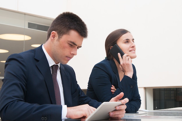 Colleagues using tablet and calling on phone at desk outdoors