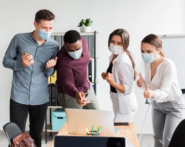 Colleagues at work in the office during pandemic wearing masks and looking at laptop
