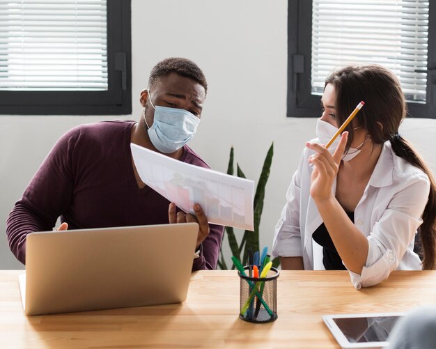 Коллеги на работе в офисе во время пандемии в медицинских масках