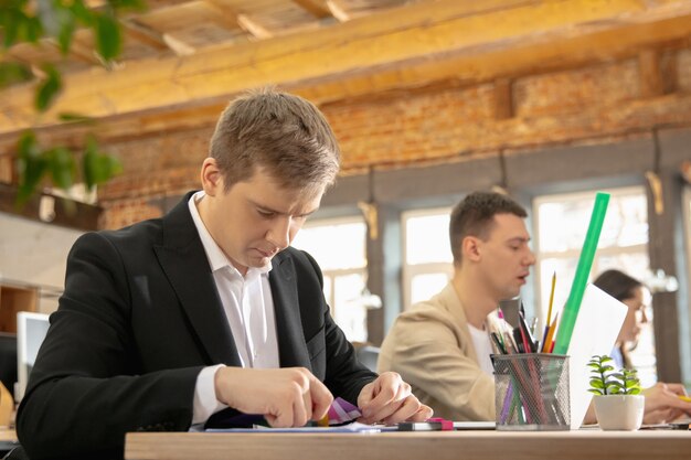 Colleagues working together in a office using modern devices during creative meeting. Stationery, laptop, documents. Concept of business, office, finance, open space.