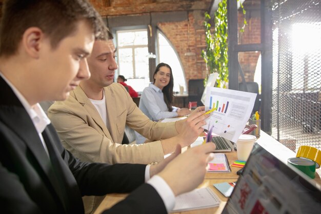 Colleagues working together in a office using modern devices during creative meeting. Stationery, laptop, documents. Concept of business, office, finance, open space.