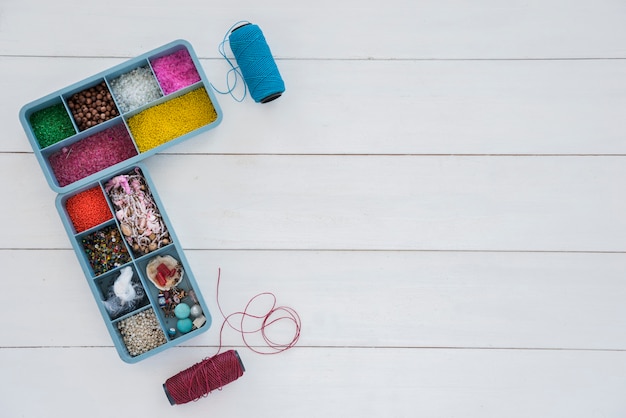 Free photo collection of beads in blue case with bright blue and purple yarn spool on white desk