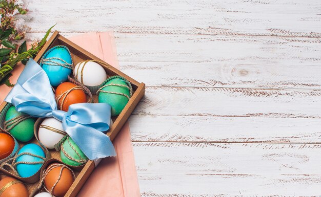 Collection of bright eggs in box on pink craft paper near plants