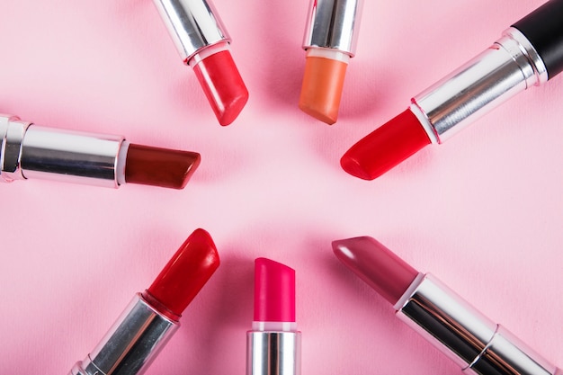 Collection of various colorful lipsticks on pink surface