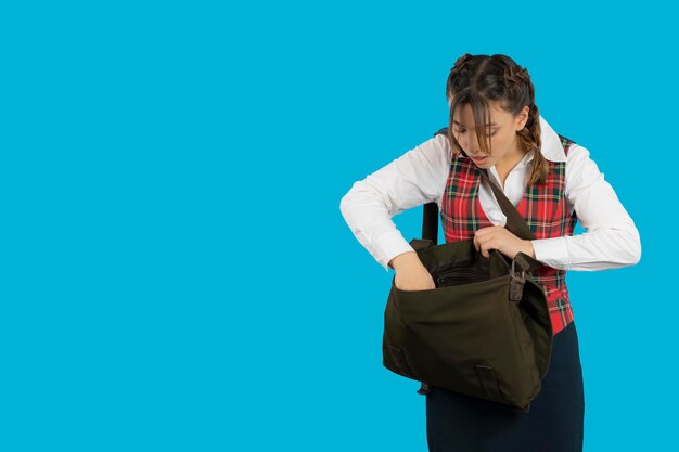 Девушка из колледжа ищет что-то в своей сумке. Фото высокого качества