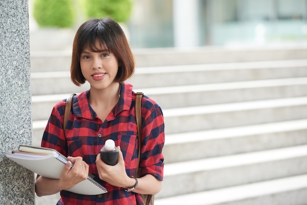 カメラ目線の大学の階段に立っている教科書を保持している大学生