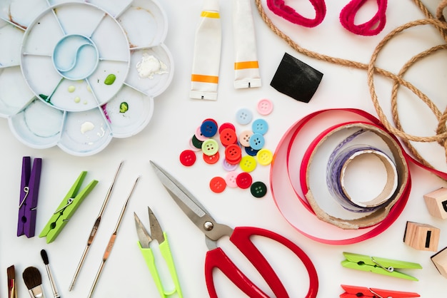 Color palette; acrylic paint tube; crochet needles; buttons; ribbon; scissor; clothespin and string isolated on white background