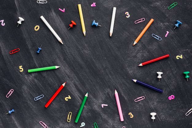 Color pencils and pushpins with paper clips scattered on blackboard