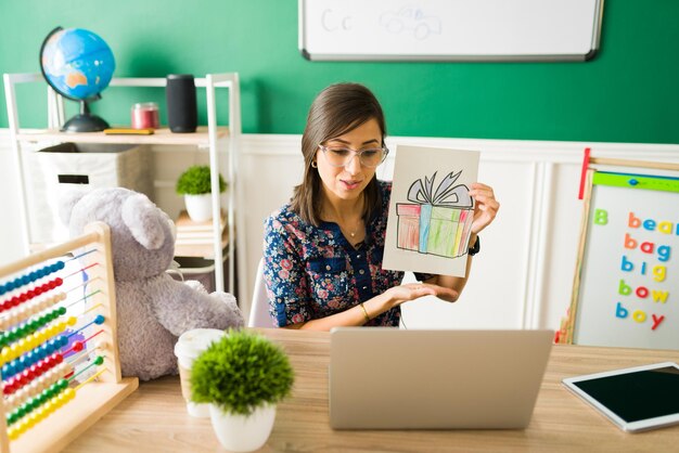 Color a picture. Hispanic teacher feeling proud and showing online the kids homework during a virtual lesson