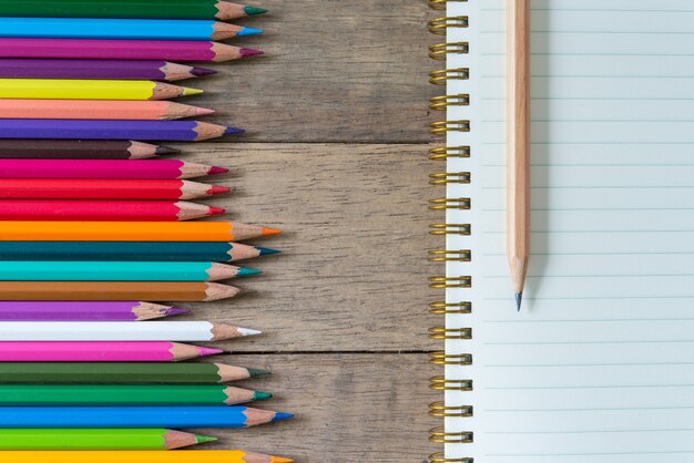 Цветные карандаши и записная книжка на деревянном