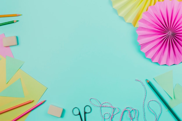 Colored pencils; rubber; paper; scissor; rope and circular paper on blue background