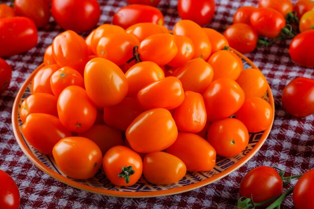 Colored tomatoes in a plate on picnic cloth, high angle view.