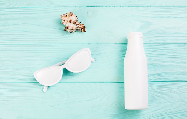 Colored white sunglasses near bottle and shell