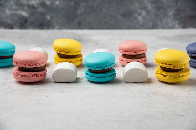 Colorful almond macarons on white table with marshmallows. 